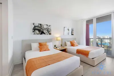 two beds in a white room with a window at Amazing Balcony Near Beach in Hallandale Beach
