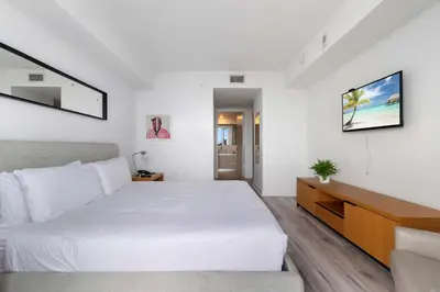 a white bedroom with a large bed and a television at Top Luxury Apartment with Pool & Gym in Hallandale Beach