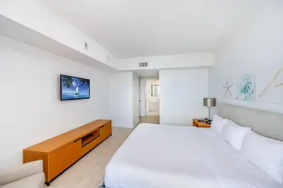 a white bedroom with a large bed and a tv at 2 Bed & 2 Bath at Beachwalk With Pool Gym on 16fl in Hallandale Beach