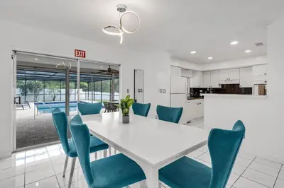 a kitchen and dining room with a white table and blue chairs at Stunning 4BR Oasis with Pool, 14 minutes to the Ocean in Hollywood