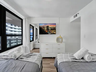 a white bedroom with two beds and a large window at Luxury Beach Condo with Exclusive Resort Amenities 1016 in Miami Beach