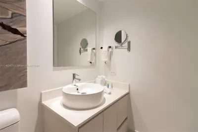 a white bathroom with a sink and a mirror at Luxury Suite on Beachwalk with Pool Gym & Beach in Hallandale Beach