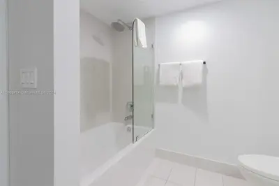 a white bathroom with a shower and a toilet at 2 Bed 2 Bath at Beachwalk with Luxury Pool and Gym in Hallandale Beach