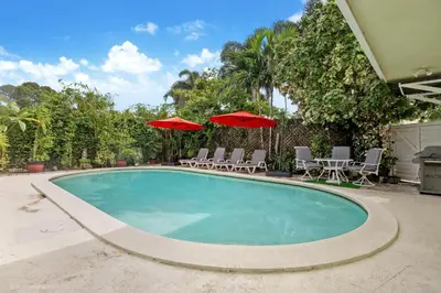 a swimming pool with two umbrellas and lounge chairs at Tropical 3BR Escape with Pool, 7 Min Drive to Beach in Hollywood