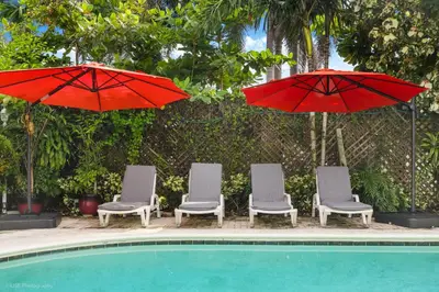 a group of chairs and umbrellas next to a pool at Tropical 3BR Escape with Pool, 7 Min Drive to Beach in Hollywood