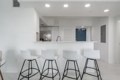 a kitchen with white stools in front of a counter at Resort-Style 1 Bed Condo with Pool Parking Rooftop & Gym in Hollywood