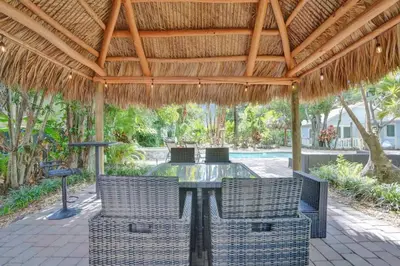 a patio with a table and chairs under a straw roof at Tropical Oasis Studio w Pool in Fort Lauderdale