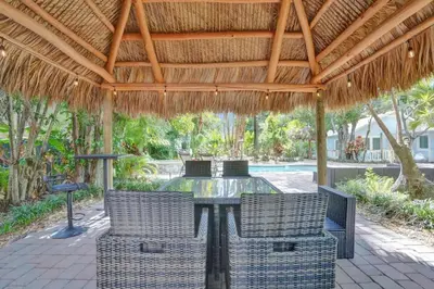 a patio with a table and chairs under a straw roof at Tropical Oasis Studio w Pool in Fort Lauderdale