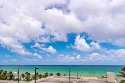 a beach with palm trees and a blue sky and clouds at Stylish Ocean Apartment with Pool in Hollywood