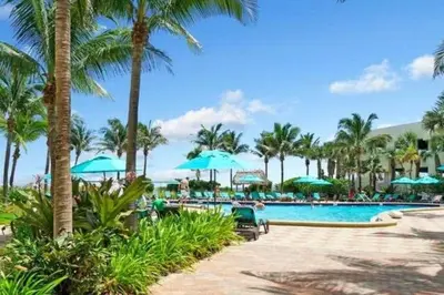 a swimming pool with palm trees and blue umbrellas at Stylish Ocean Apartment with Pool in Hollywood