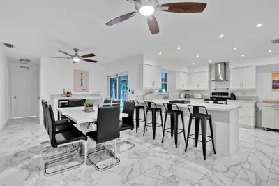 a white kitchen with a table and black chairs at Waterfront House - Solar Heated Pool, Arcade Games in Fort Lauderdale