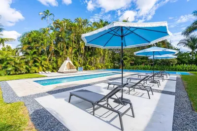 a group of chairs and umbrellas next to a swimming pool at Pickleball fun Family home near Hard Rock Stadium in North Miami