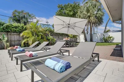 a row of chaise lounge chairs with an umbrella at The Zen Den - Heated pool - One mile to heart of The Drive in Fort Lauderdale