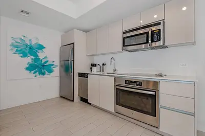 a kitchen with white cabinets and a stainless steel refrigerator at 1 Bedroom & Kitchen at Beachwalk Luxe Pool - Gym in Hallandale Beach