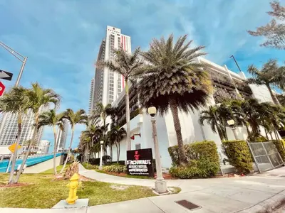 a building with palm trees and a yellow fire hydrant at Amazing Studio at Beachwalk with Pool & Gym in Hallandale Beach