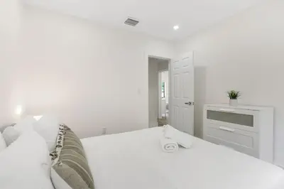 a white bedroom with a white bed with a clock on it at Charming 4BR Oasis with Saltwater Pool and Parking in North Miami