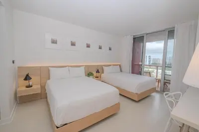 a white bedroom with two beds and a window at Studio Luxury Ocean Views Apt in Hallandale Beach in Hallandale Beach
