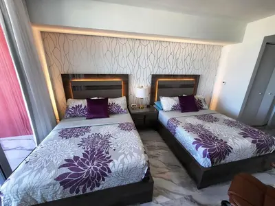two beds in a hotel room with purple and white sheets at The Royal Studio of Beachwalk in Hallandale Beach
