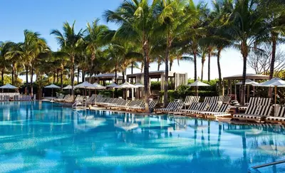 a swimming pool with chairs and umbrellas and palm trees at SOUTH BEACH Stunning Studio in Miami Beach