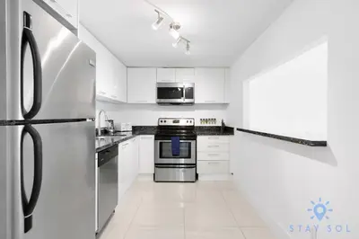 a white kitchen with stainless steel appliances and white cabinets at Apartment 2BR 2BTH - Free Parking in Sunny Isles Beach