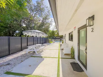 a patio with two white benches and a fence at Designer 1BR Retreat Heart of Miami Pool in Miami