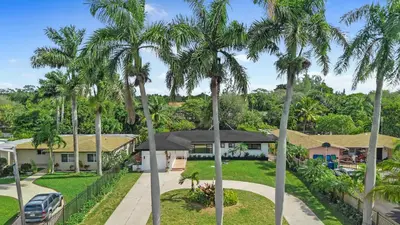 a house with palm trees in front of a driveway at Luxury Miami Waterfront Retreat with Private Dock in Golden Glades
