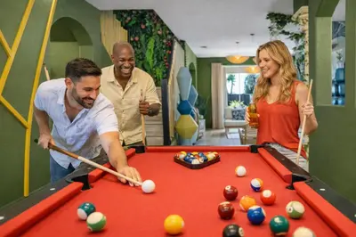 a group of people standing around a pool table at Luxury Glow Villa Miami - 4K Private Cinema, Heated Pool & Spa, Game Room - 5BR Lakefront Estate for 12 Guests in Hammocks