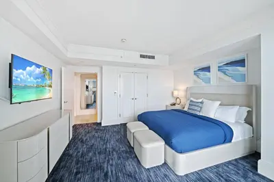 a white bedroom with a blue bed and a tv at Ritz-Carlton Luxury Oceanfront 2BR on 16th Floor in Fort Lauderdale