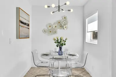 a white dining room with a table with a vase of flowers at Dream Hollywood Beach Retreat With Jacuzzi and Fire Pit in Dania Beach