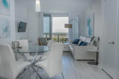 a white living room with a glass table and white chairs at 2B 2B Beachfront Pool Gym and Restaurant in Hallandale Beach