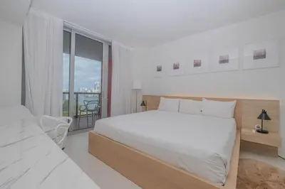 a white bedroom with a large bed and a balcony at Enjoy Miami 2B 2B pool beach and Aventura Mall in Hallandale Beach
