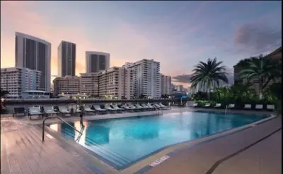 a large swimming pool with chairs and a city at BeachWalk Studio Apmt 2 Beds with Beach Service 2103 in Hallandale Beach