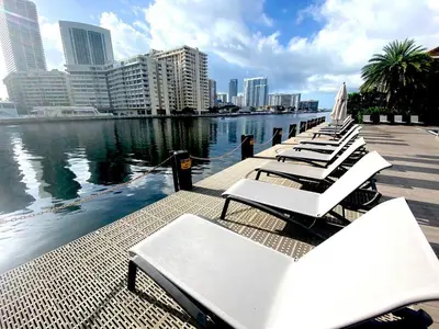a row of white lounge chairs next to the water at Enjoy Miami Beach Pool and Restaurant 2B 2B 2007 in Hallandale Beach