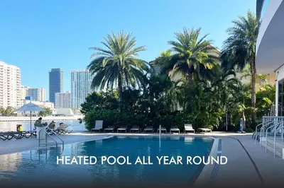 a heated pool all year round with palm trees and buildings at Miami Beach Cozy 1B with Pool and Beach Service 1506 in Hallandale Beach