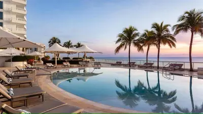 a swimming pool with chairs and palm trees and the ocean at Oceanfront Ritz-Carlton 1 Bedroom Luxury Residence in Fort Lauderdale