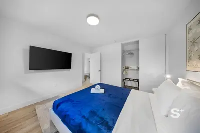 a white bedroom with a blue bed and a flat screen tv at Sleek 1-BD Miami Apt Gym, BBQ, Free Parking in Miami
