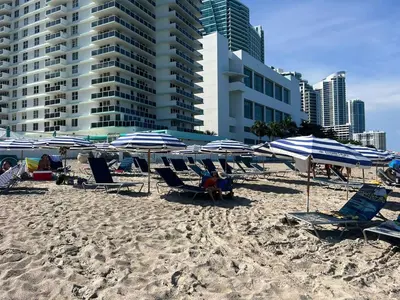 a beach with blue and white umbrellas and chairs at BeachWalk Studio Apmt 2 Beds w Beach Service in Hallandale Beach