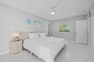 a white bedroom with a large bed and a night stand at Beach Home in Victoria Park in Fort Lauderdale