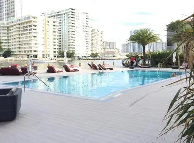 a large swimming pool with lounge chairs and buildings at Cozy 1BR Retreat wPool BeachService & Full Kitchen in Hallandale Beach