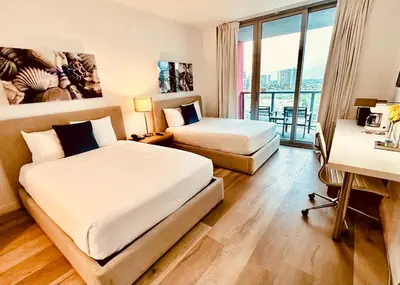 a hotel room with two beds and a desk and a window at Studio with Service Beach and Pool Hallandale Beach in Hallandale Beach