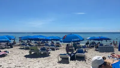 a beach with chairs and blue umbrellas and people at Amazing Studio at Hallandale Beach with service beach in Hallandale Beach
