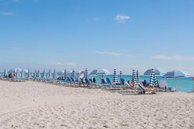 a group of chairs and umbrellas on a beach at Studio 2 beds queen, pool, gym and service beach in Hallandale Beach