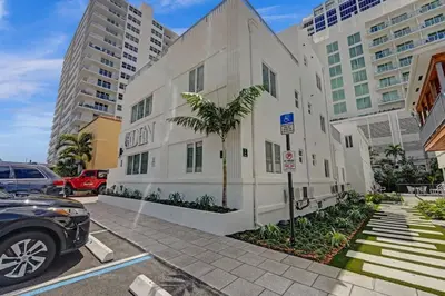 a white building with a palm tree in a parking lot at Eden Collection Studio Steps to Beach in Fort Lauderdale