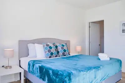 a white bedroom with a blue bed with two lamps at Family-Friendly Townhouse Getaway Near Top Attractions in Golden Glades