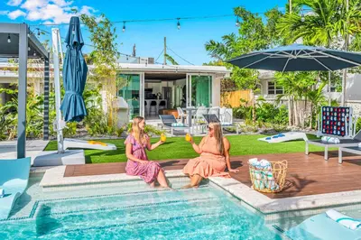 two women sitting next to a swimming pool with drinks at Waterfront Heated pool Lime Key Two in Fort Lauderdale