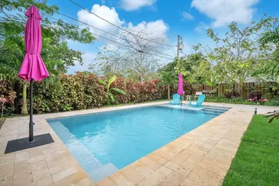 a swimming pool with two chairs and an umbrella at The Frolics -Stunning Wilton Manors Pool Home in Fort Lauderdale