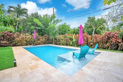 a swimming pool with two blue chairs and a pink umbrella at The Frolics -Stunning Wilton Manors Pool Home in Fort Lauderdale