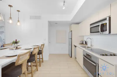 a white kitchen with a long counter and some chairs at Stylish -2BR Apartment -Balcony & Pool in Hallandale Beach