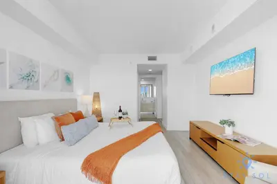 a white bedroom with a large bed and a tv at Amazing 1BR Apt View & Balcony - Pool & Gym in Hallandale Beach