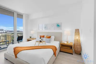 a white bedroom with a large bed and a balcony at Amazing 1BR Apt View & Balcony - Pool & Gym in Hallandale Beach